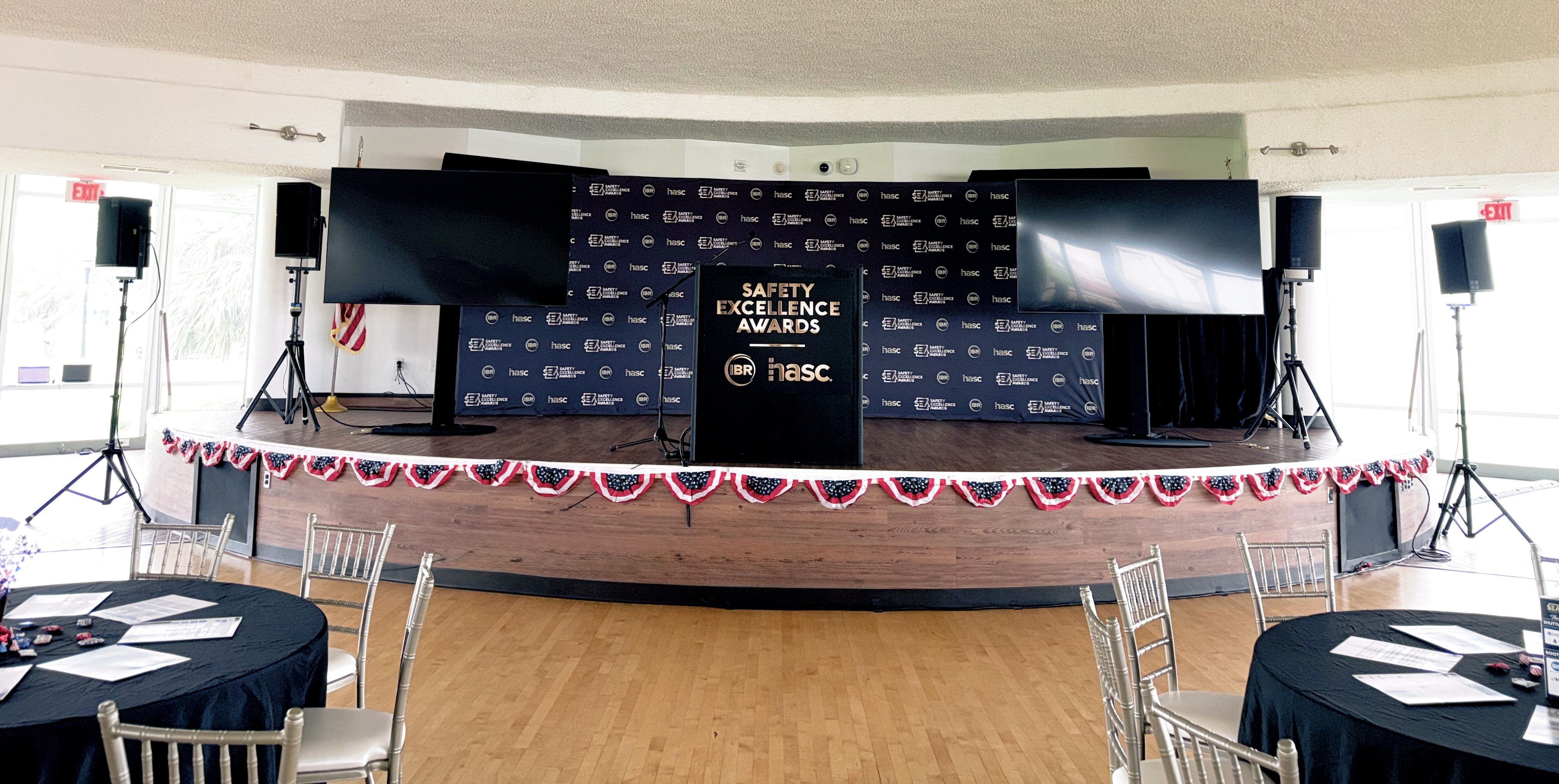 Stage setup for Safety Excellence Awards ceremony with patriotic bunting, podium, and round tables awaiting attendees.
