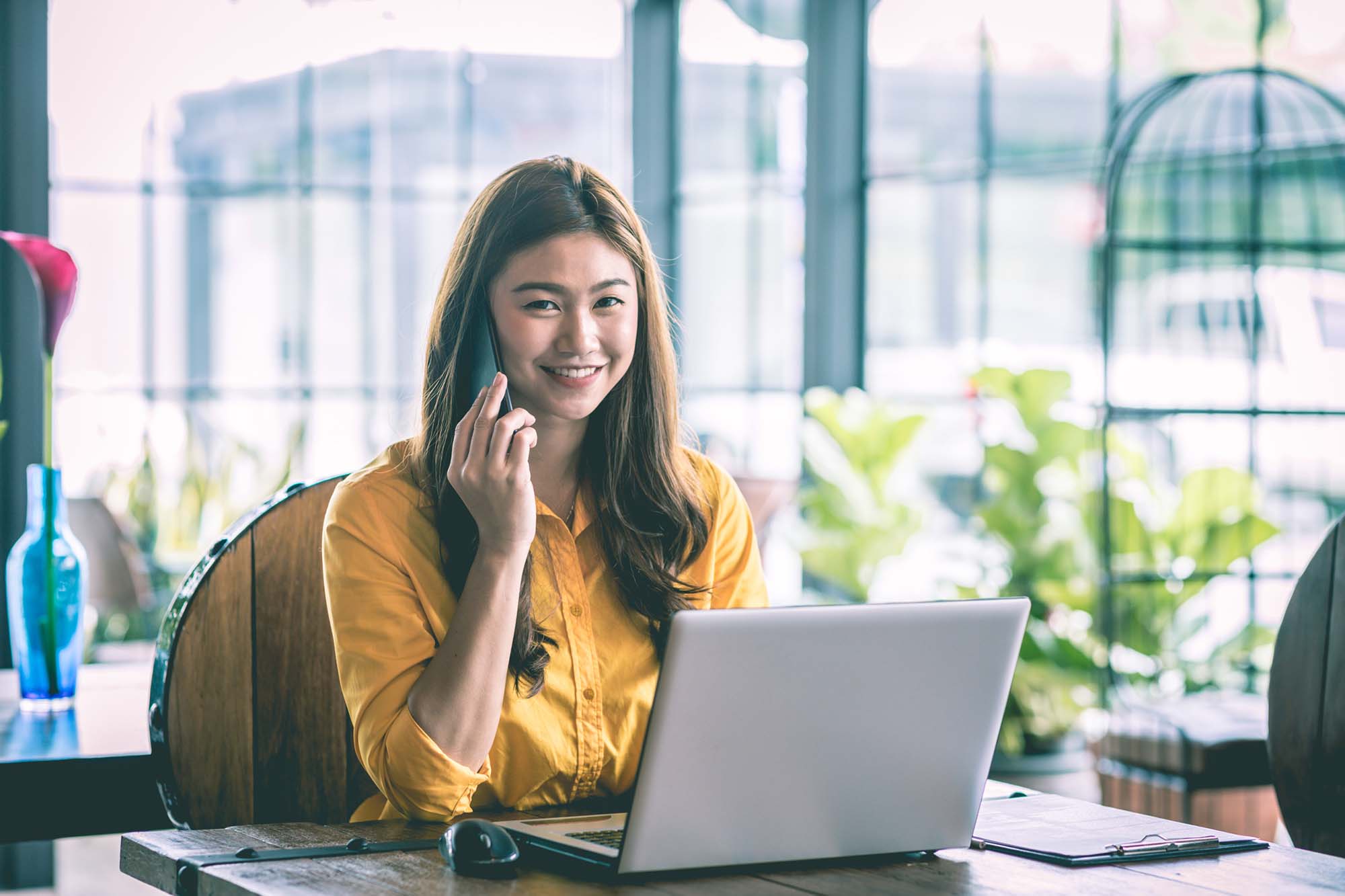 Smiling woman talking on mobile phone while sitting in front of a laptop