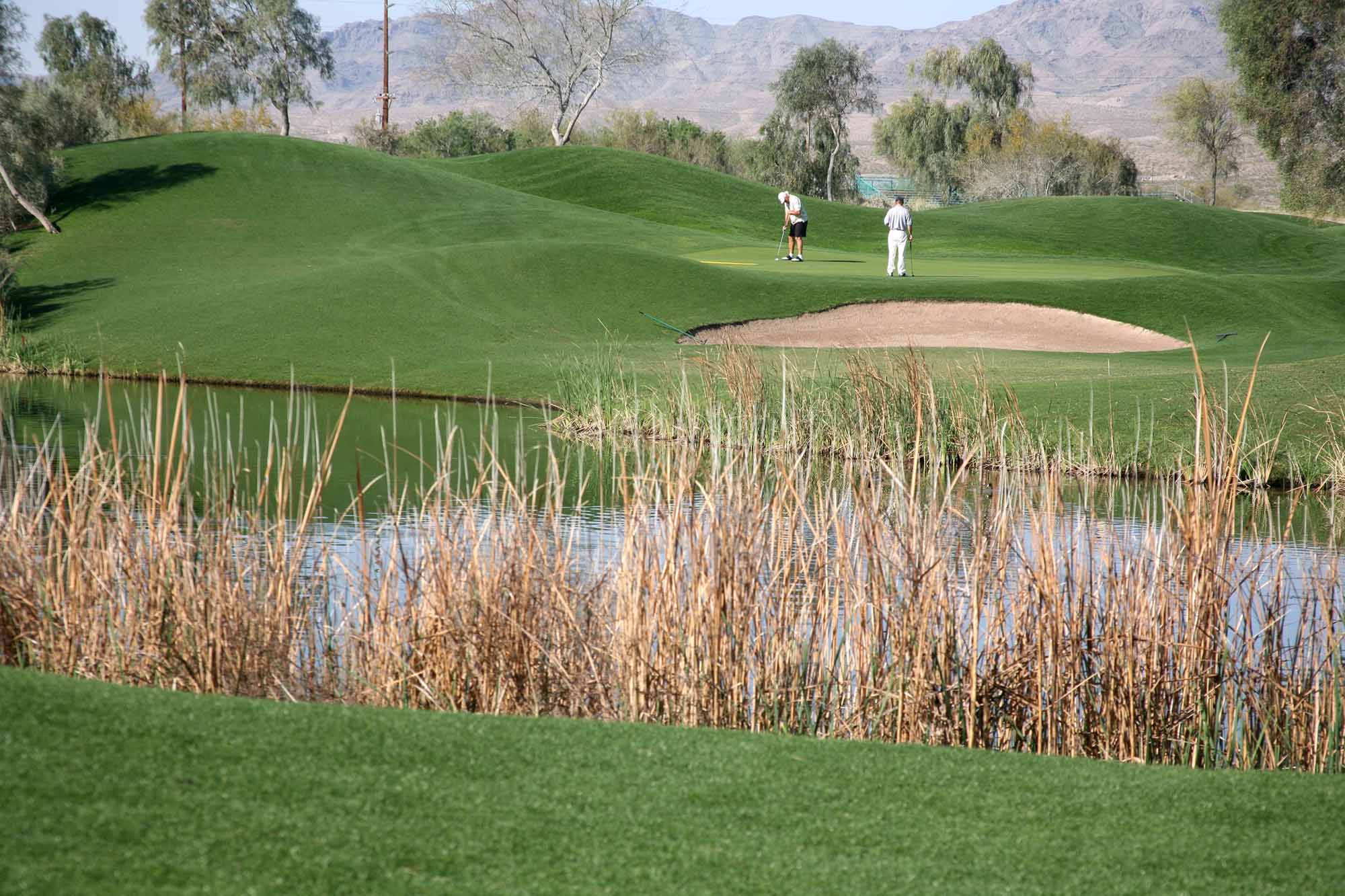 Two golfers on the putting green, with a sand trap and water hazard in the foreground