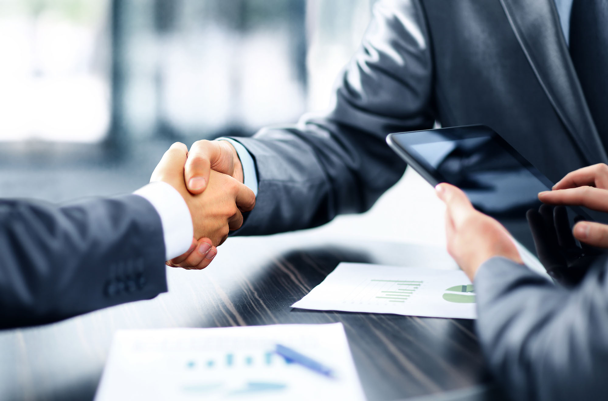 Two members shaking hands while a third interacts with a tablet